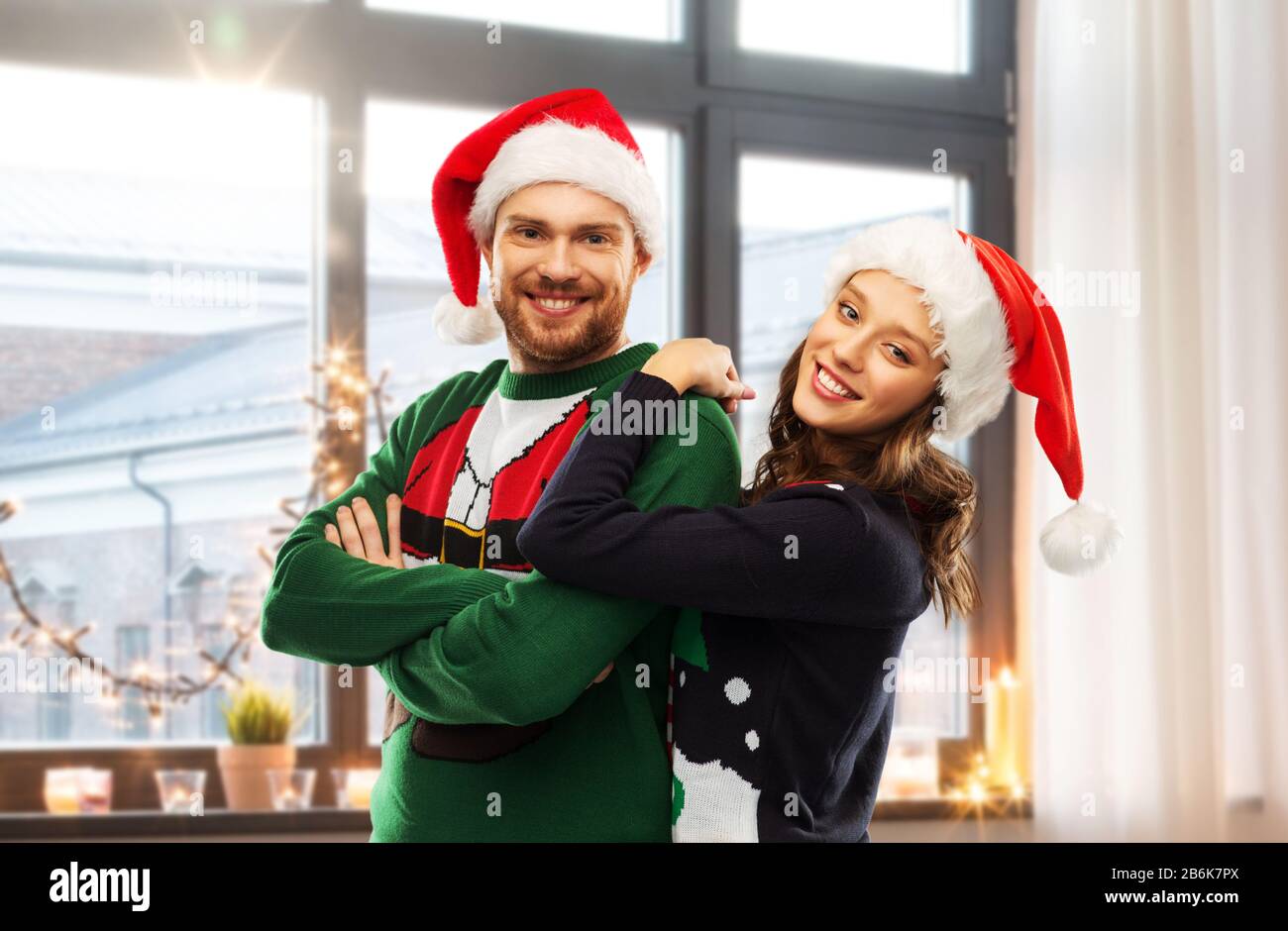 christmas, people and holidays concept - portrait of happy couple in santa  hats at ugly sweater party over home room background Stock Photo - Alamy