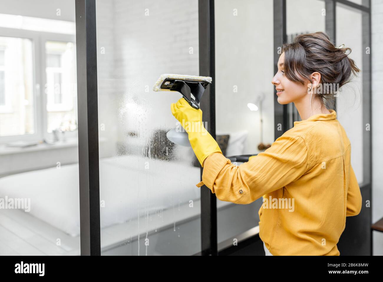 Happy woman washing glass partitions with a special cleansing device at home. Concept of a professional housekeeping Stock Photo