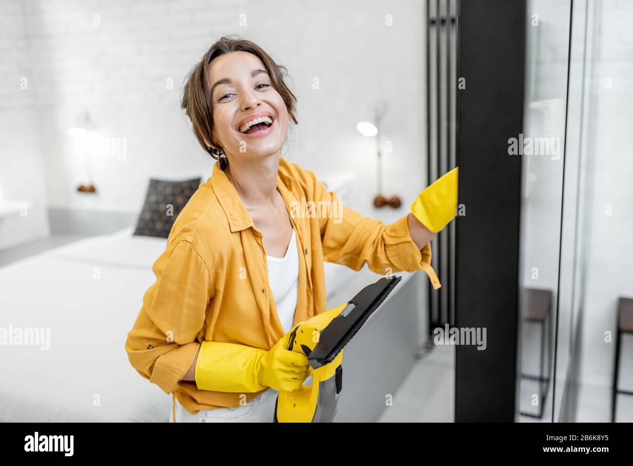 Portrait of a happy woman washing glass partitions with a special cleansing device at home. Concept of a professional housekeeping Stock Photo
