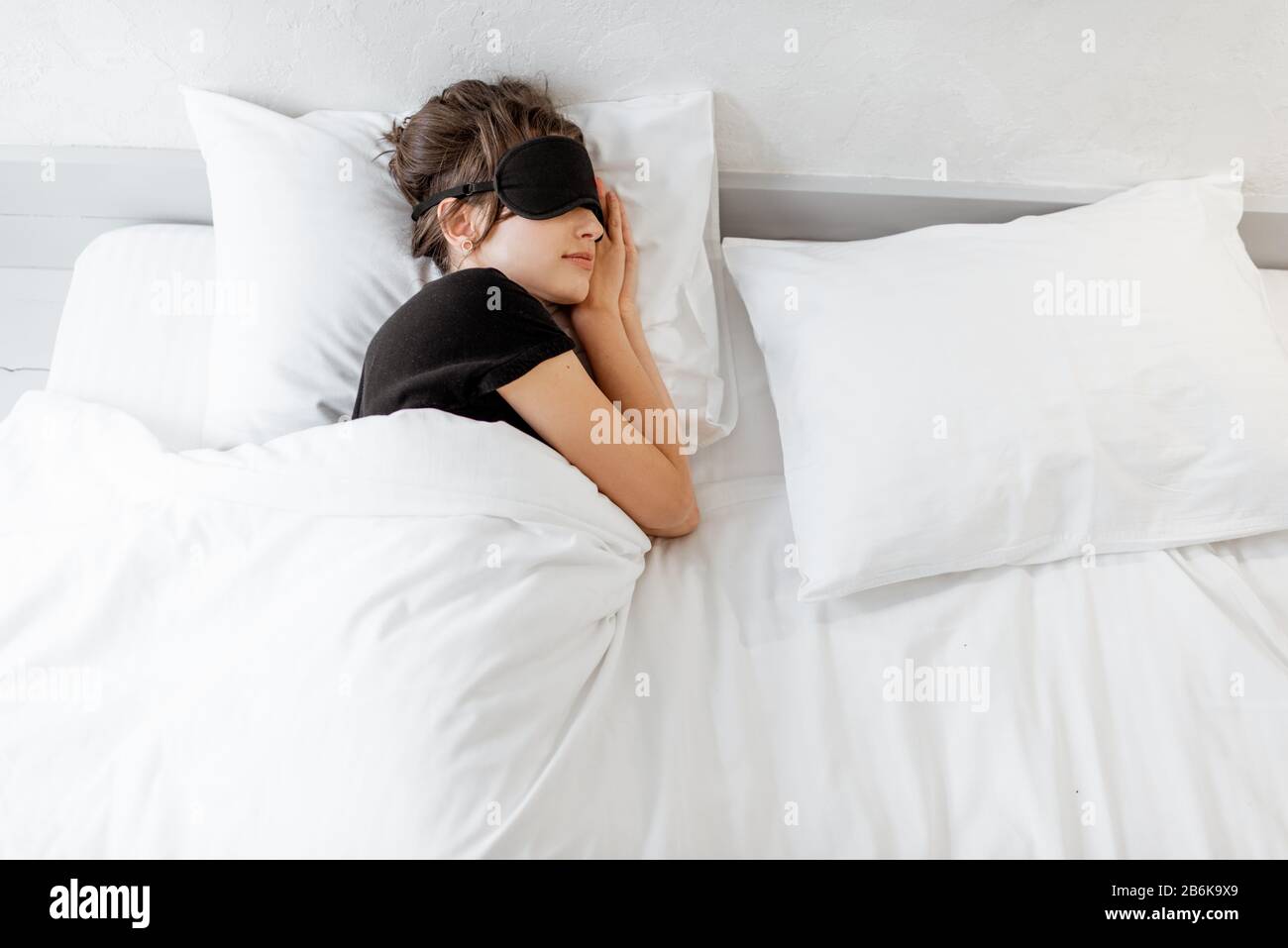 Woman lying with a sleeping mask in bed covered with white sheets in
