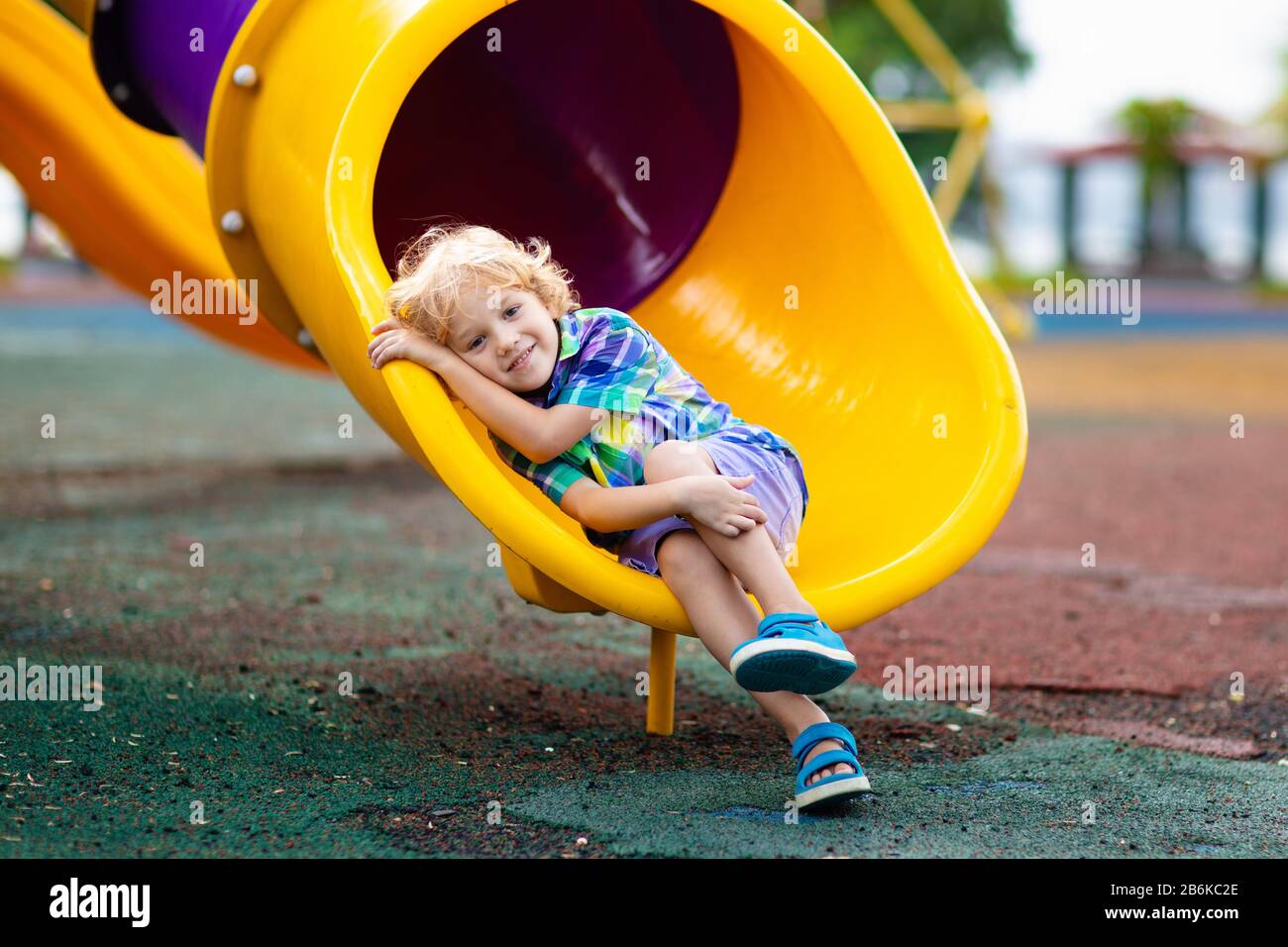 Child playing on outdoor playground. Kids play on school or kindergarten yard. Active kid on colorful slide and swing. Healthy summer activity for chi Stock Photo