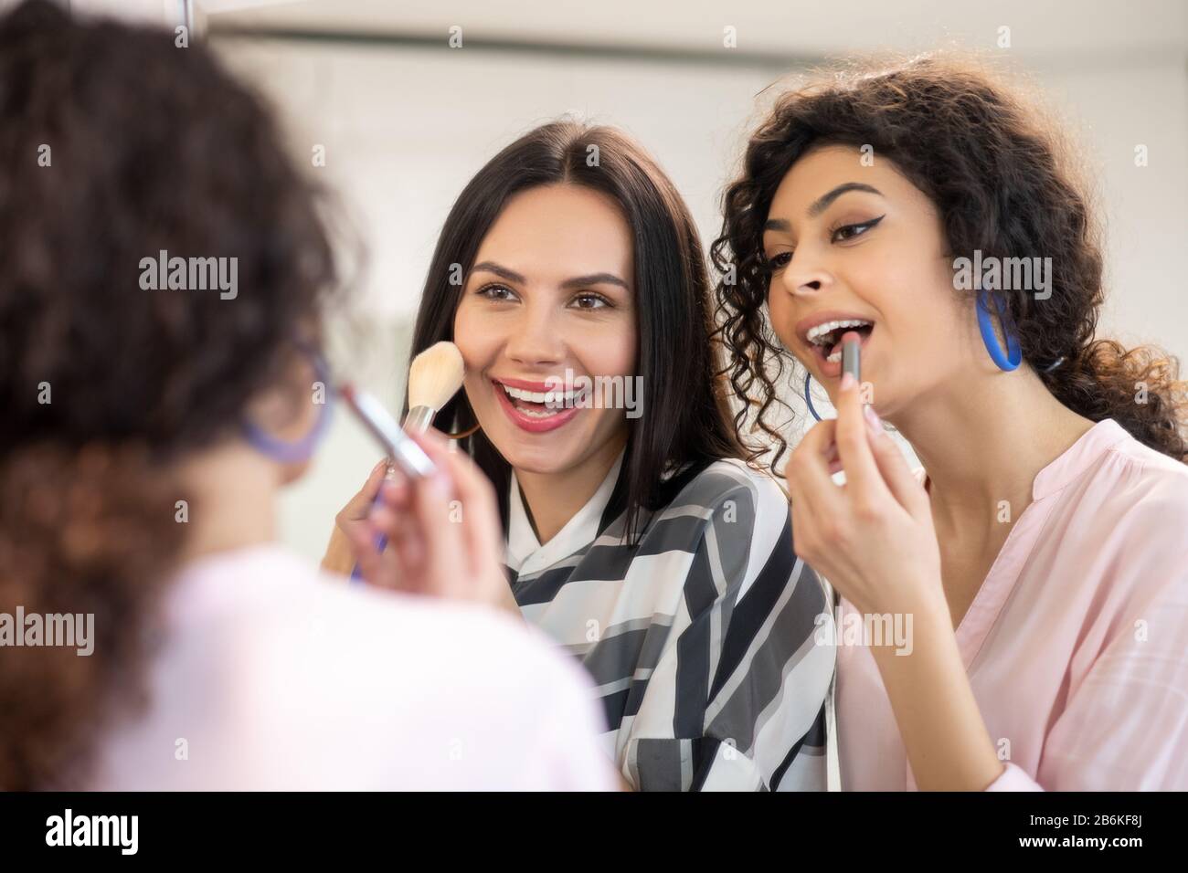 Two dark-haired women doing make up and feeling amused Stock Photo