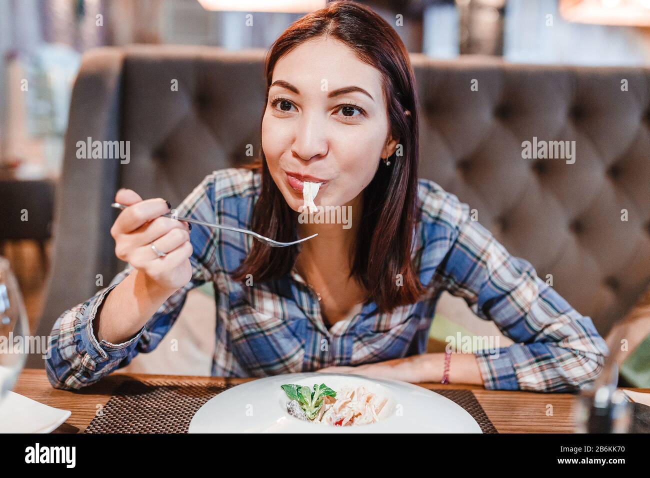 Eastern woman eating spaghetti pasta with fork in luxury restaurant