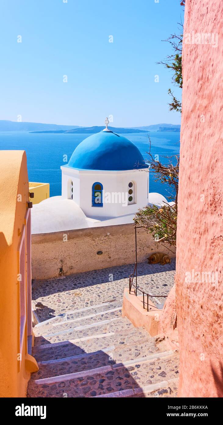 Street and Greek orthodox church with blue dome by the sea in Oia town in Santorini island, Greece Stock Photo