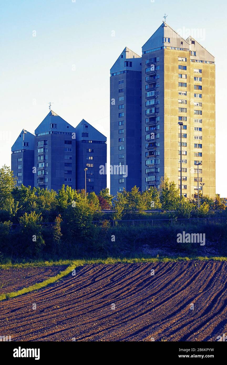 Freshly plowed field and residential buildings in background lit by setting sun. Urbanism, agriculture and sustainability concepts Stock Photo