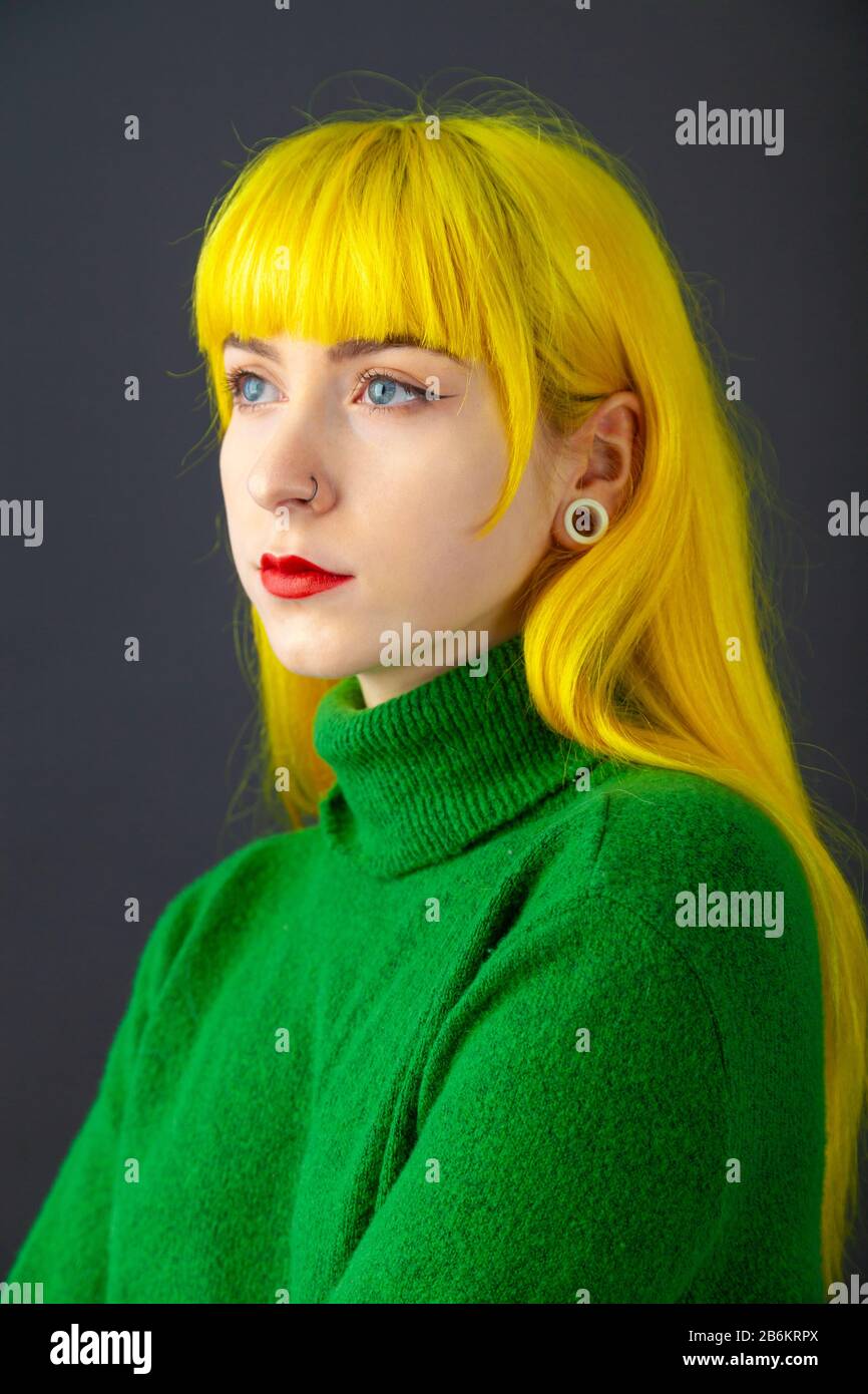 Fashion shot of a young woman with bright yellow hair and wearing a bright green jumper against a white background. Stock Photo