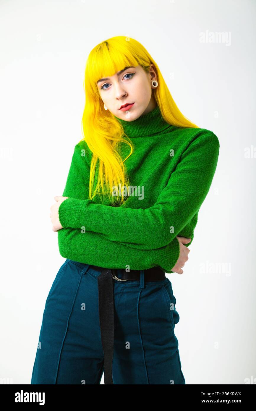 Fashion shot of a young woman with bright yellow hair and wearing a bright green jumper against a white background. Stock Photo