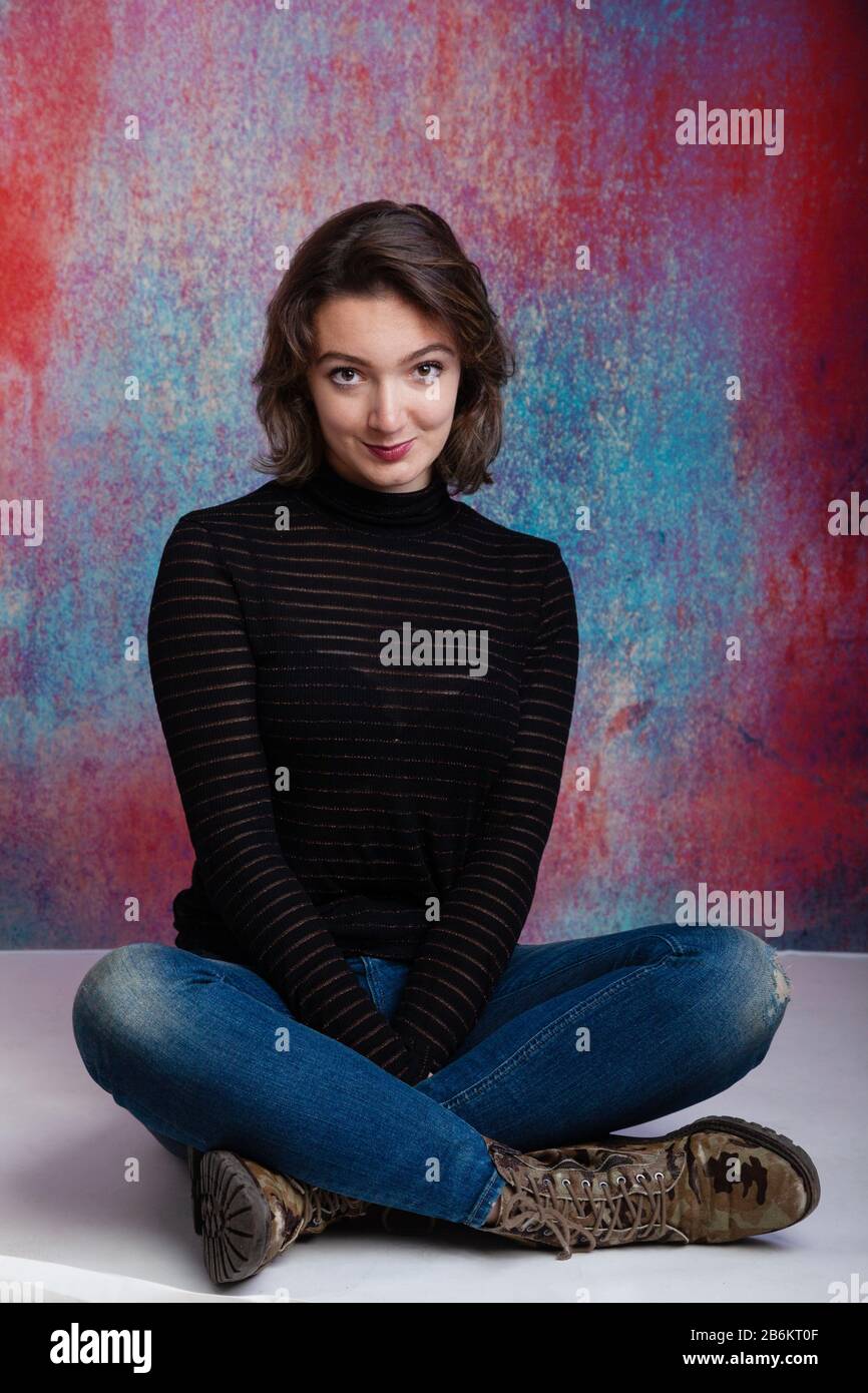 Twenty year old woman sitting crossed legged wearing a long sleeved jumper and blue jeans. Stock Photo