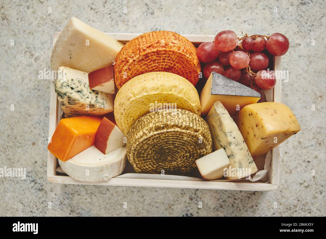 Fresh and delicious different kinds of cheeses placed in wooden crate with grapes Stock Photo
