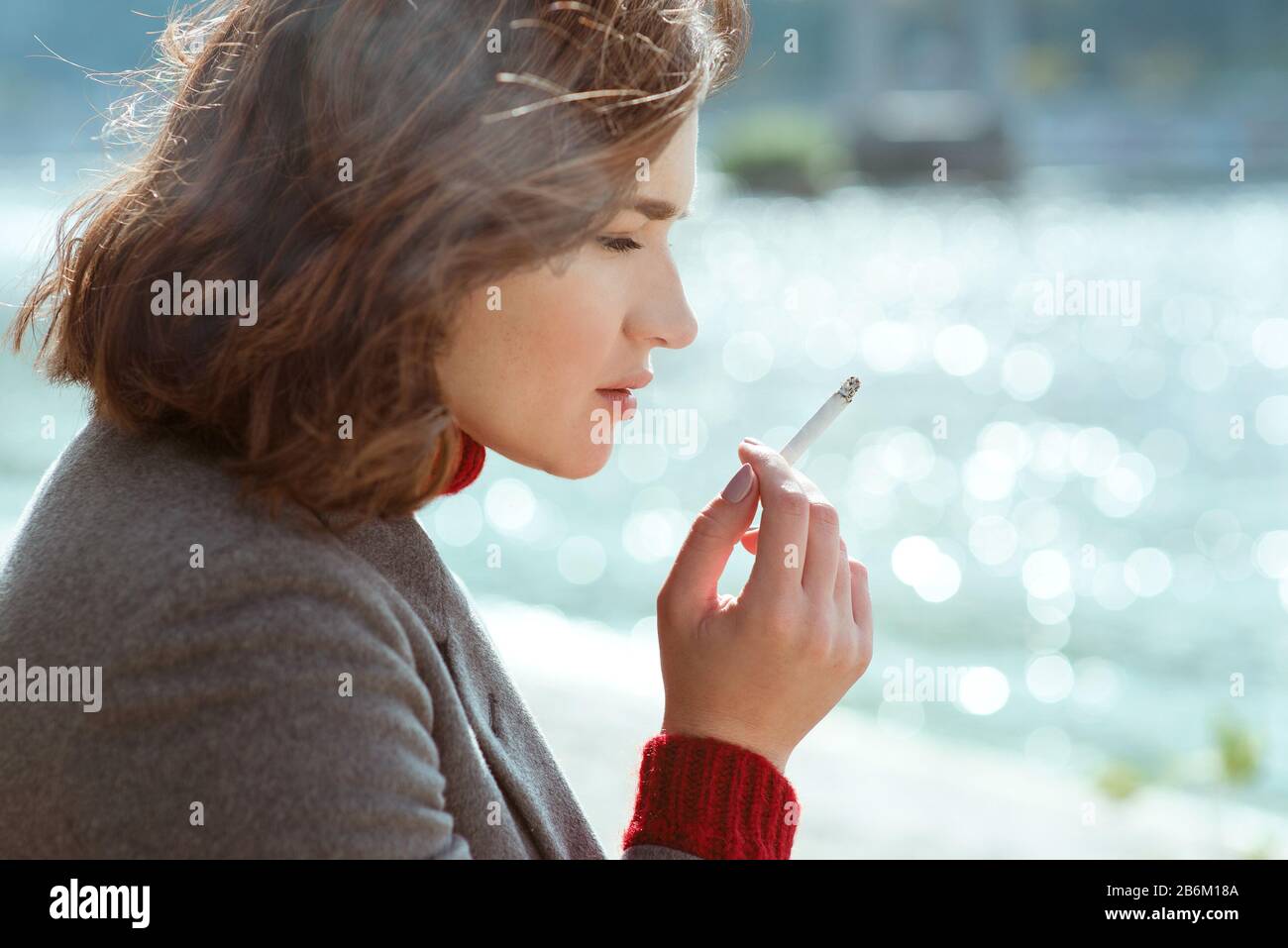 beautiful stylish sad stressful young woman in sweater and coat smoking
