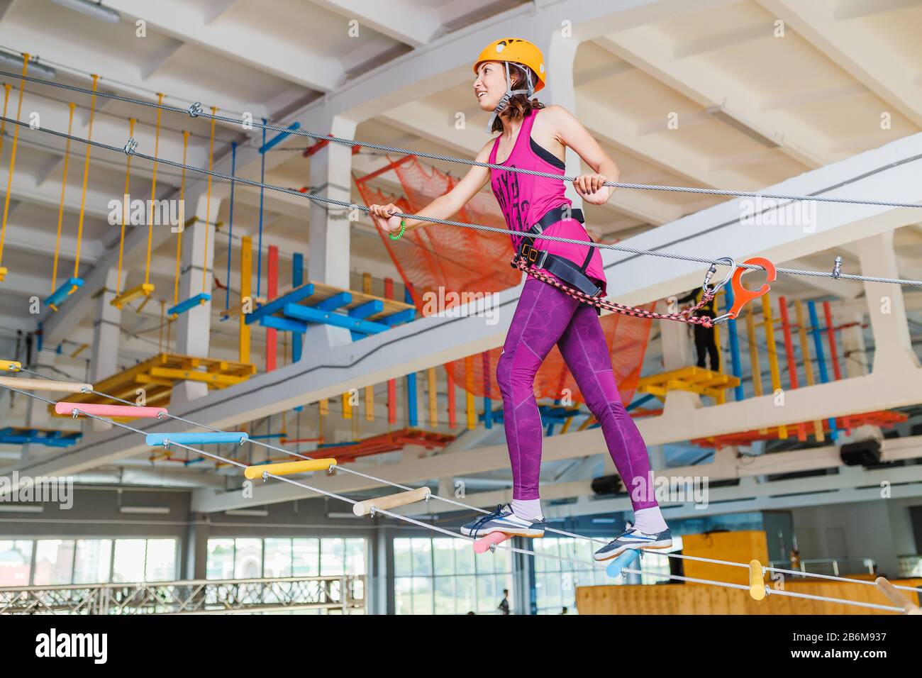 20 AUGUST 2017, UFA, RUSSIA, TRAMPOLINE CENTER 'FLYPARK': Young woman walking on a ladder in rope park gym indoors Stock Photo