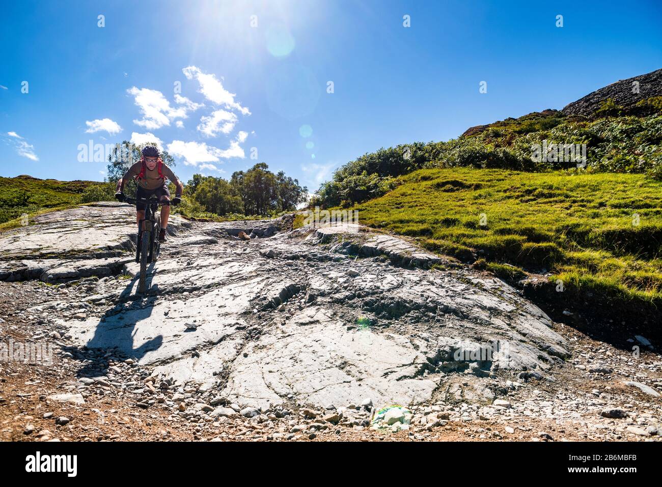 Cyclist (on e-bike) on exposed bedrock on the descent from Knotts into Little Langdale in the English Lake District Stock Photo
