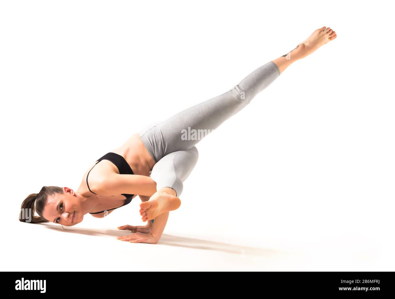 Flexible woman in mahamudra yoga pose indoors. Female yogi sitting in the  great gesture asana over purple wall. Advance practitioner stretching with  hands to big toe. Healthy lifestyle concept Stock Photo