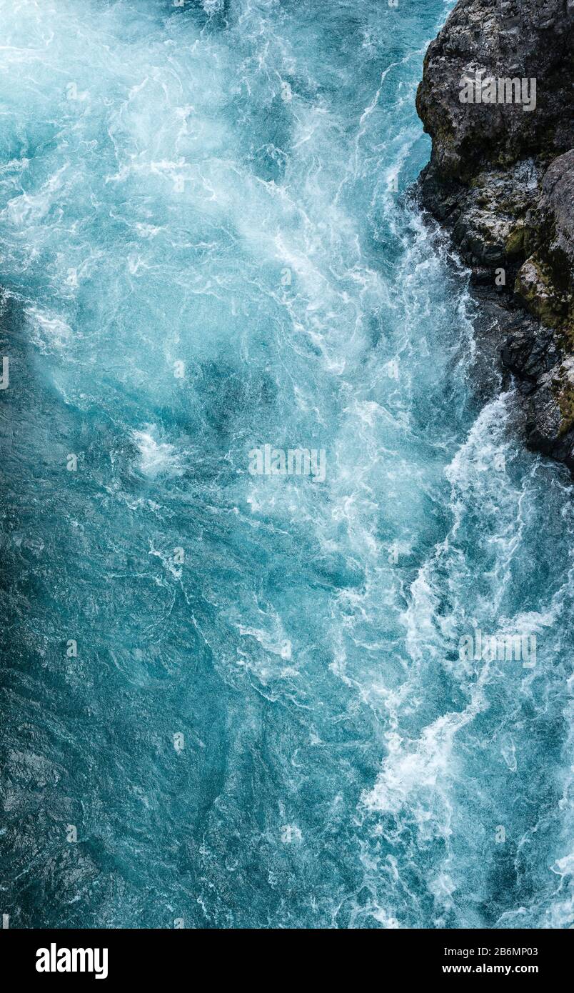 The ice blue glacier water of the river Hvítá pouring over the waterfall of Barnafoss in west Iceland, between cliffs of black lava Stock Photo