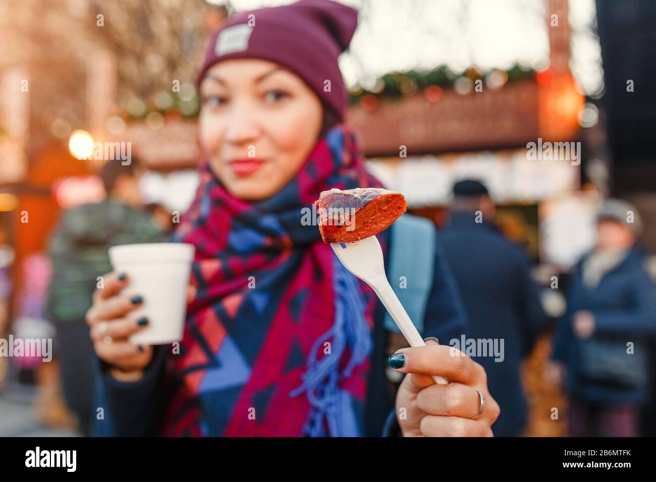 young woman traveler snacks a sausage with a hot drink on the street of a European city in the winter Stock Photo