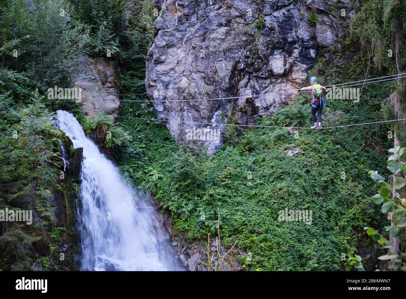 Woman crossing the suspended wire bridge towards Talbach waterfall, on a via ferrata route in Zillertal valley, Austria. Stock Photo