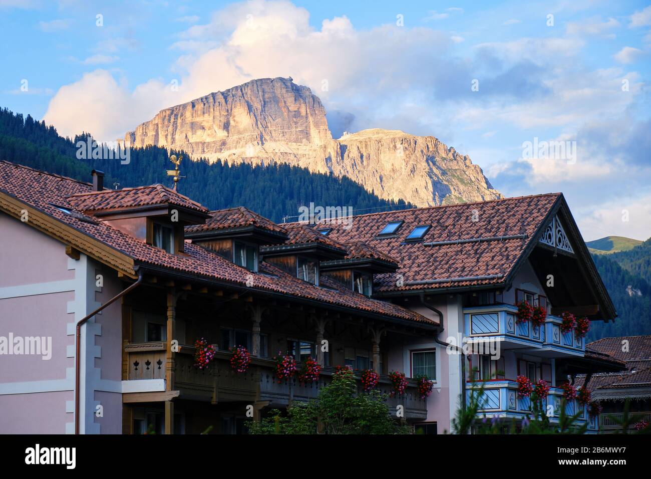 Traditional Italian house in Campitello di Fassa, with Dolomites mountain peaks lit by orange sunset light in the background. Stock Photo