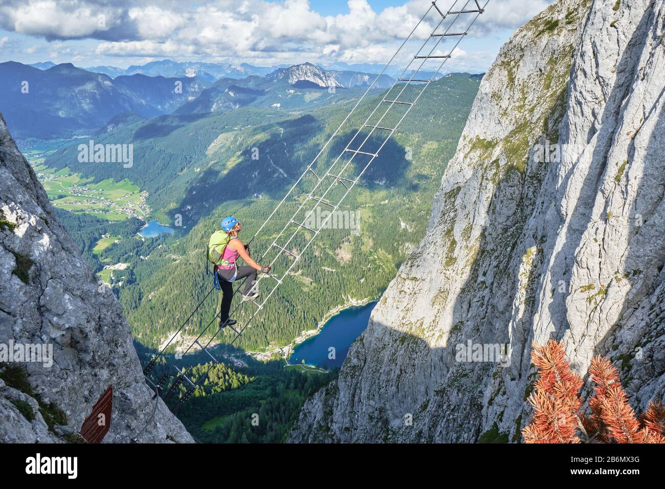 Woman on via ferrata ladder above Gosau lake, on the Intersport Klettersteig Donnerkogel route, in Austria. High angle view on a Summer day. Stock Photo