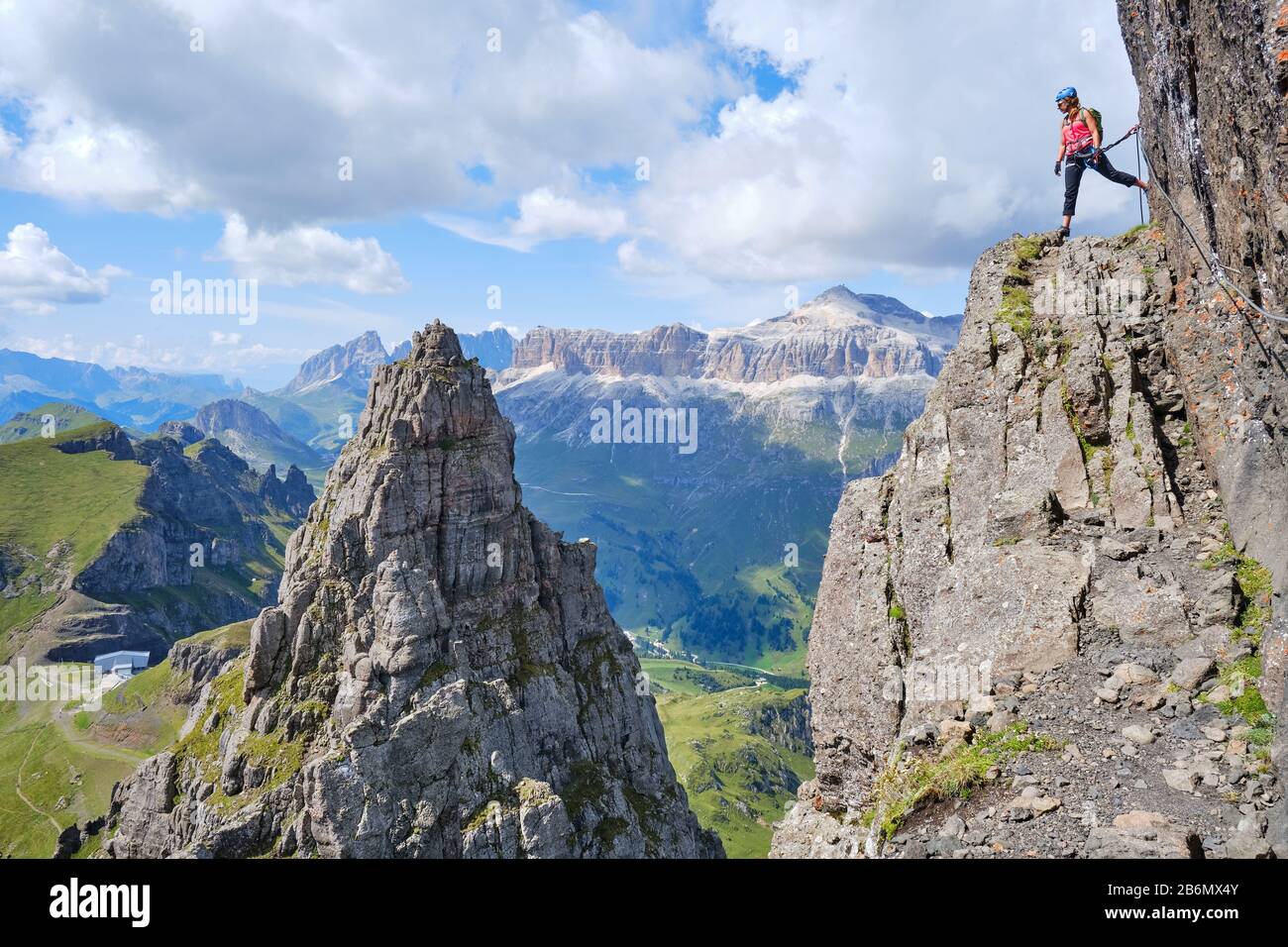 Woman on via ferrata Delle Trincee (meaning Way of the trenches), high above impressive pointy rock peak, with Sella group in the distance as backgrou Stock Photo