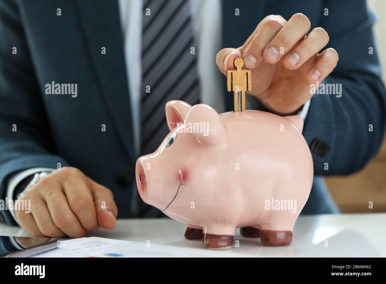 Male manager putting small wooden human figure into piggybank Stock Photo