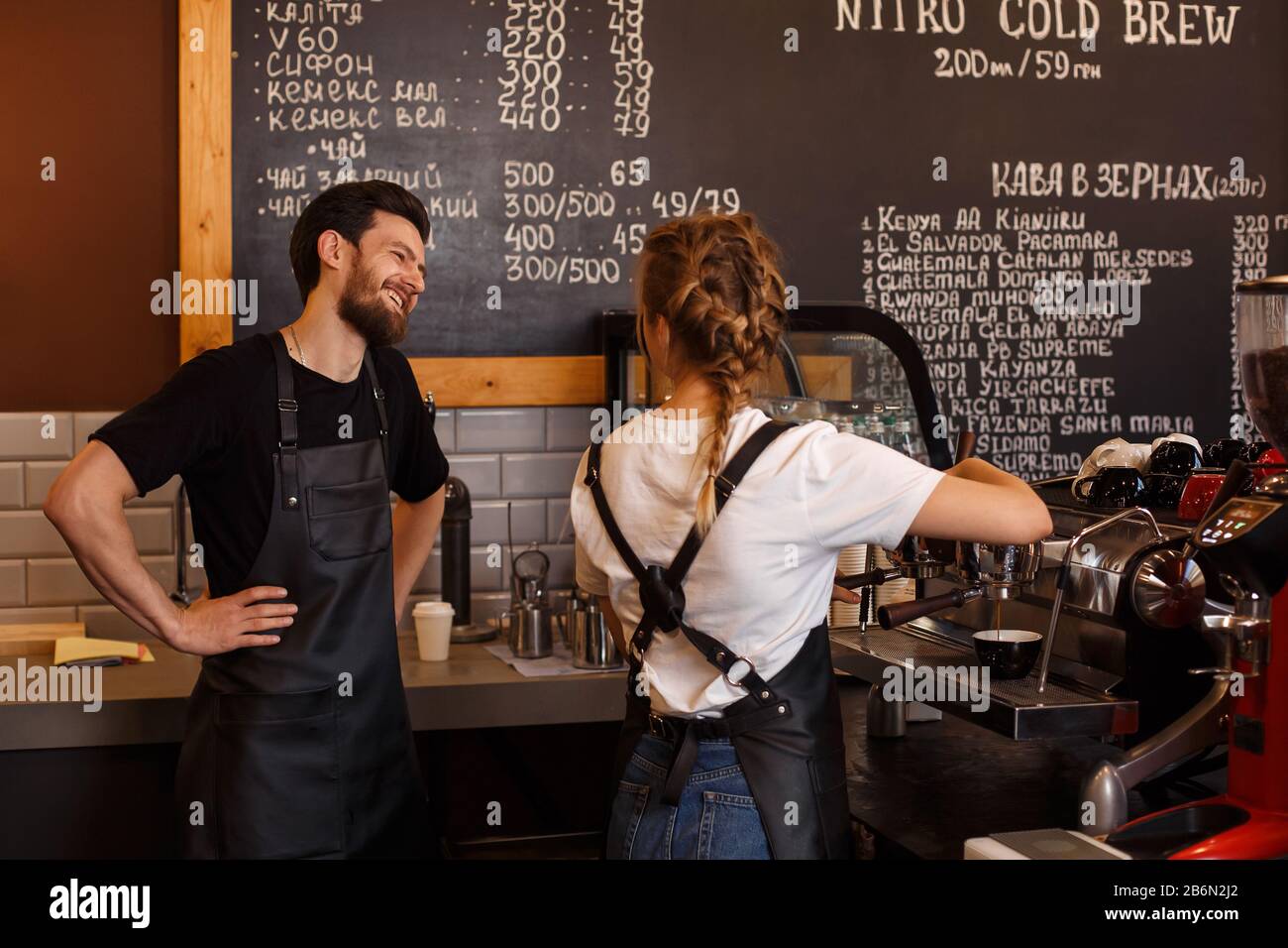 Two young smiling barista at work. Professional barista team brewing coffee using coffee machine