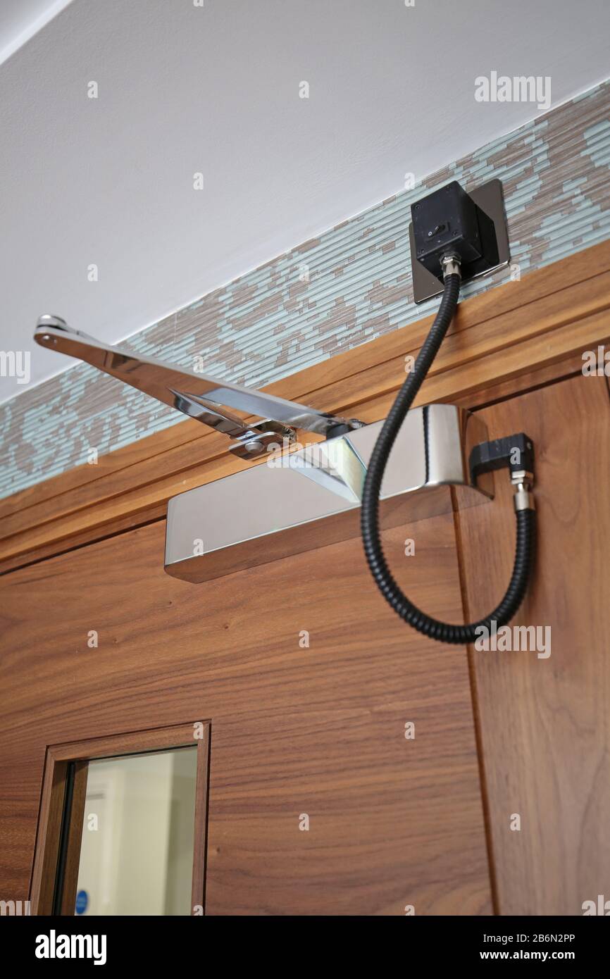 An electronically controlled door closer mounted on a hardwood corridoor fire door in a block of luxury apartments. Chrome finish. Stock Photo