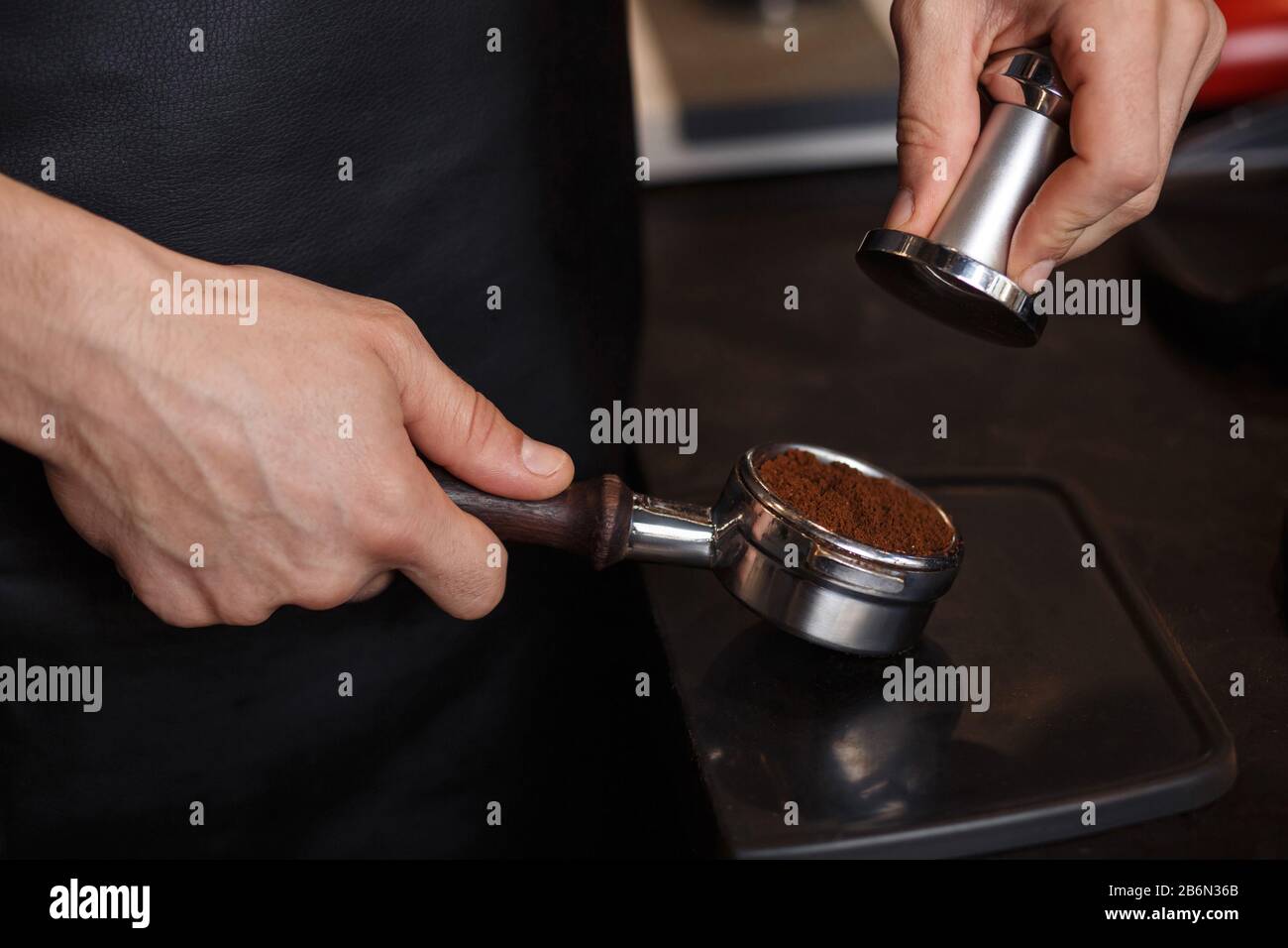 Young male barista pressing ground coffee into bottomless portafilter