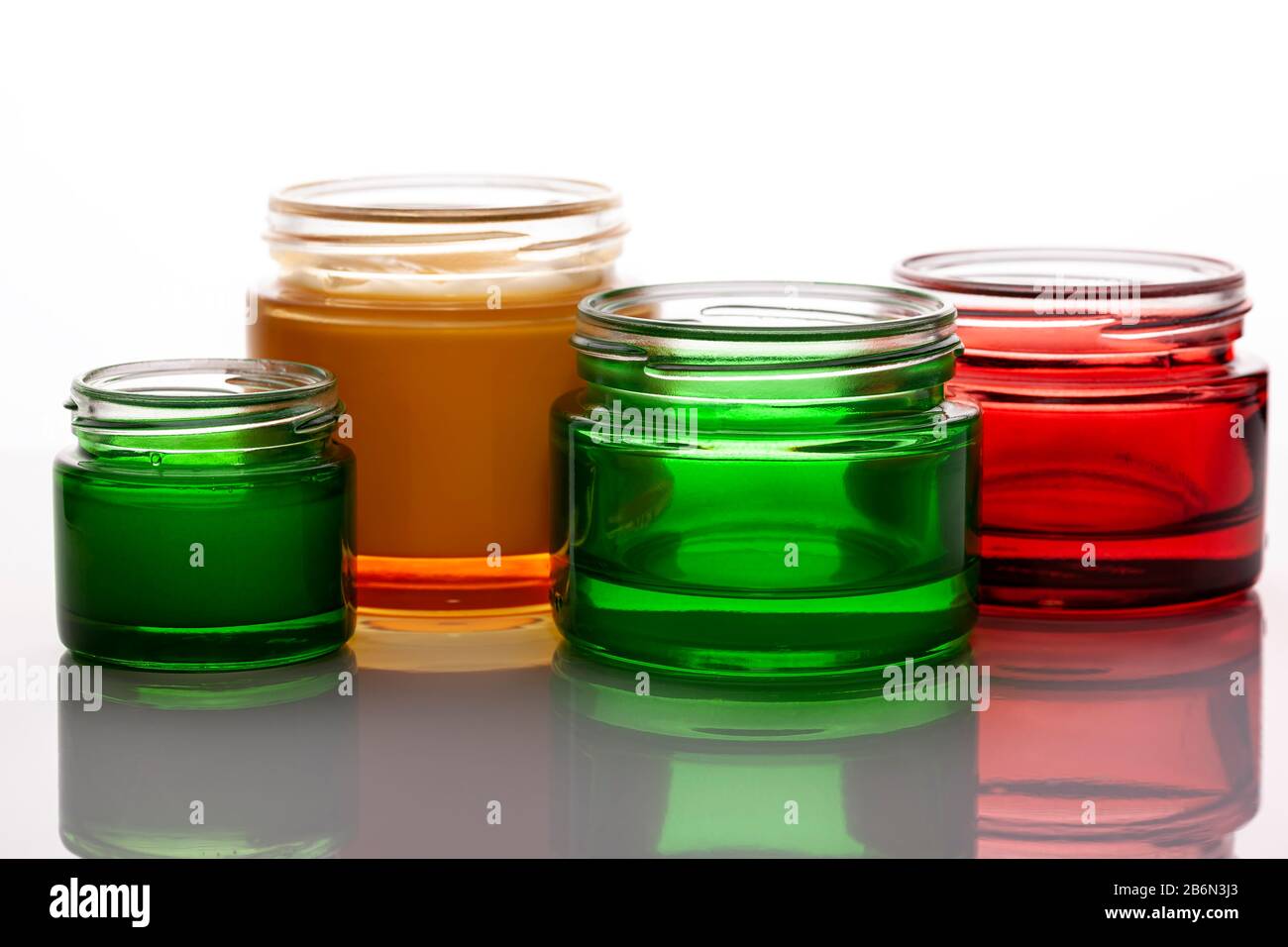 Colorful glass cosmetic jars empty and full with cream on bright background. Reflection on a glossy surface. Background light Stock Photo