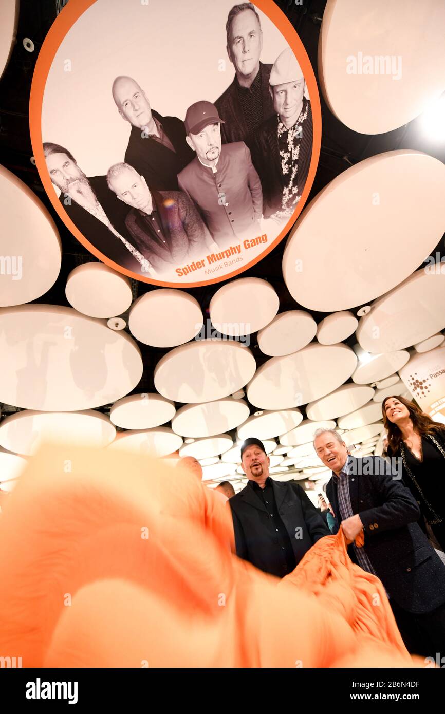 Munich, Germany. 11th Mar, 2020. Barny Murphy (l) and Günther Sigl, musicians of the band Spider Murphy Gang, as well as Karen Webb, presenter, are standing in the Stachus Passages under a ceiling circle in the Sky of Fame with a photo of the band Spider Murphy Gang. In the Sky of Fame, on the ceiling circles of the Stachus Passages, there are pictures of Munich personalities. Murphy, Sigl unveiled their picture on 11.03.2020. Credit: Tobias Hase/dpa/Alamy Live News Stock Photo