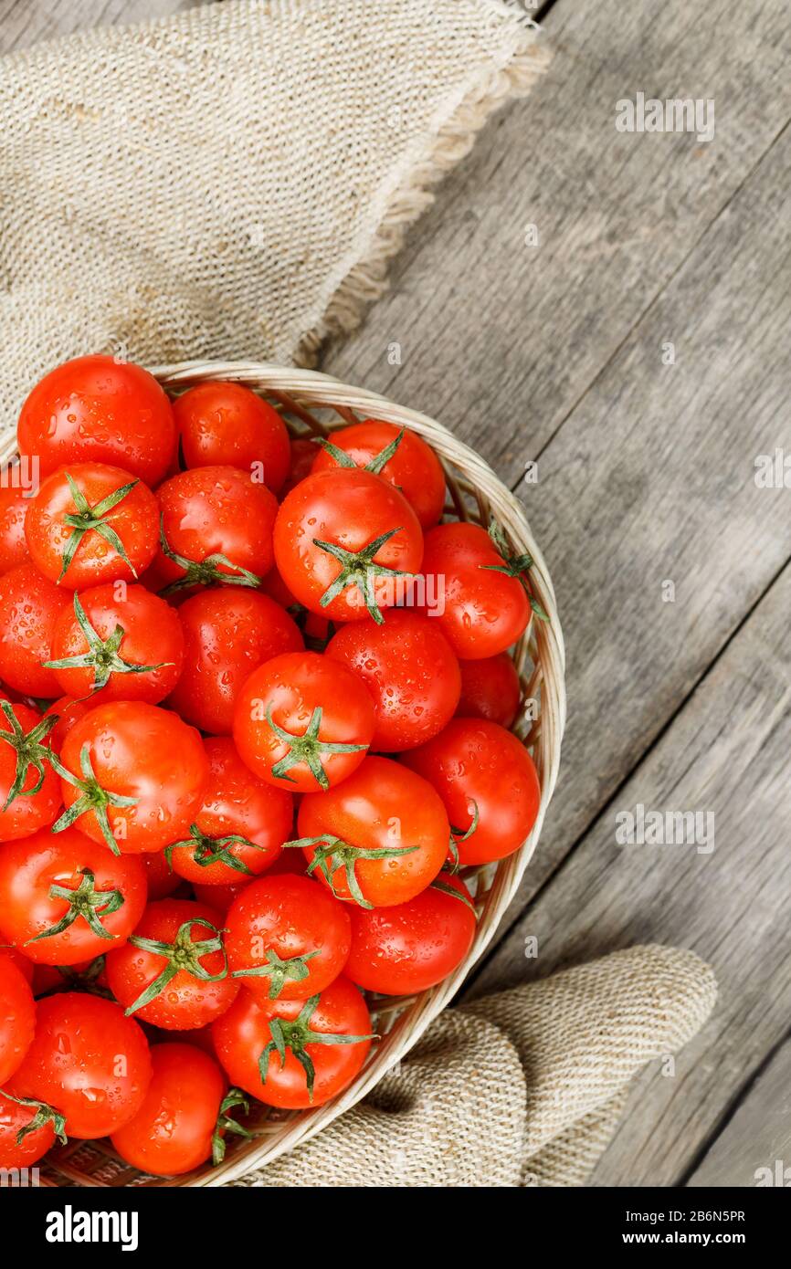 Small red tomatoes in a wicker basket on an old wooden table. Ripe and ...