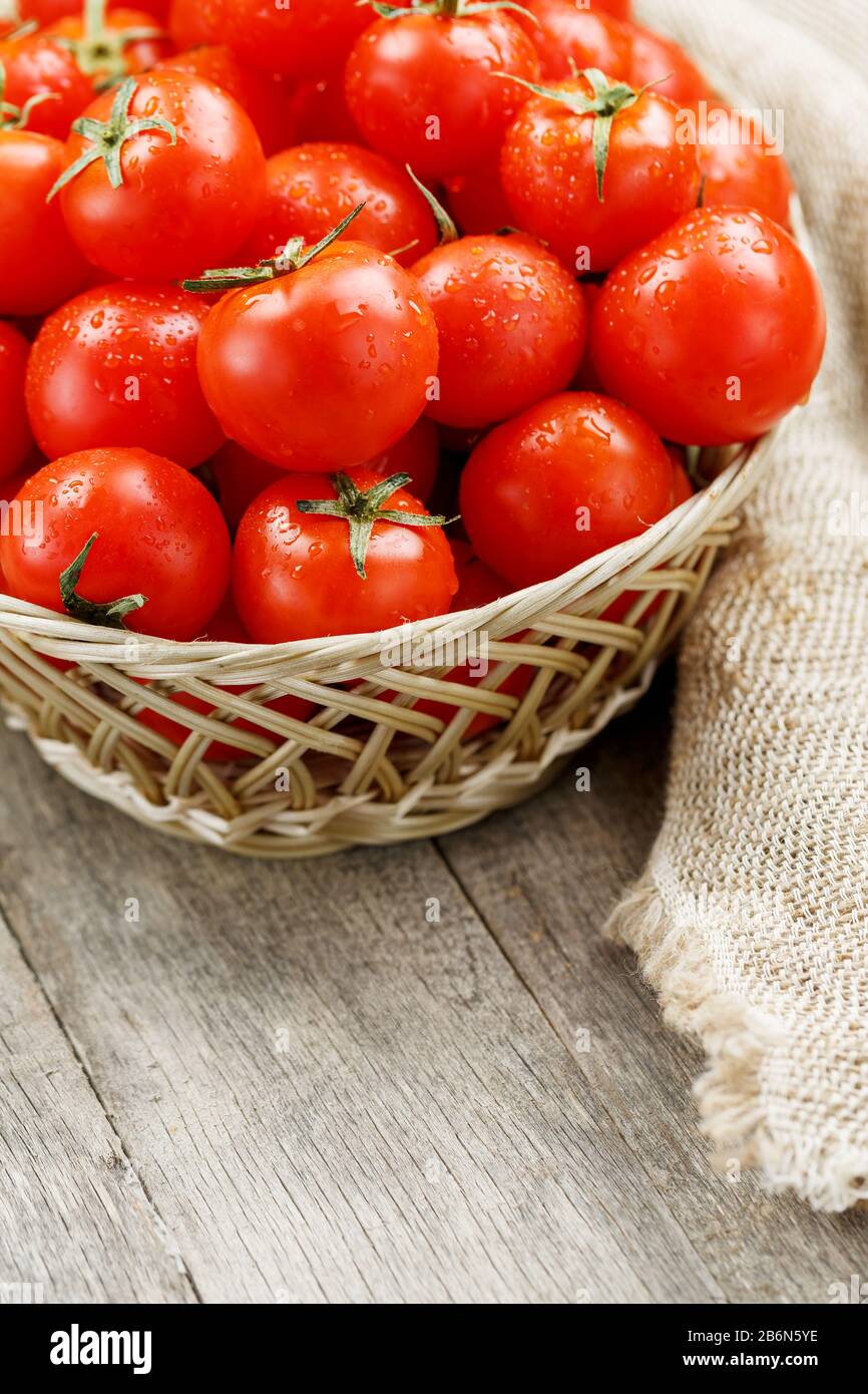 Small red tomatoes in a wicker basket on an old wooden table. Ripe and ...