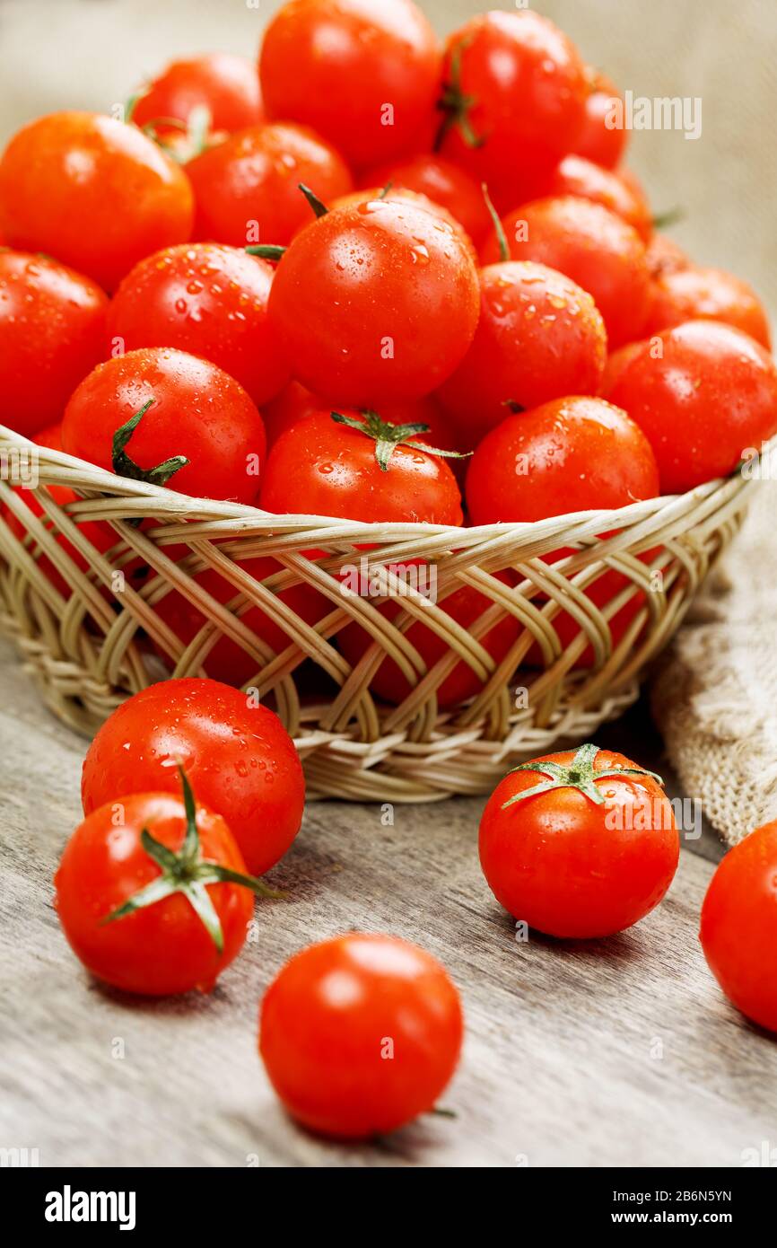 Small red tomatoes in a wicker basket on an old wooden table. Ripe and ...