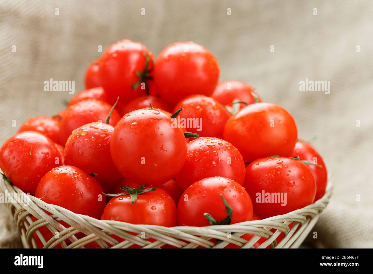 Small red tomatoes in a wicker basket on an old wooden table. Ripe and ...