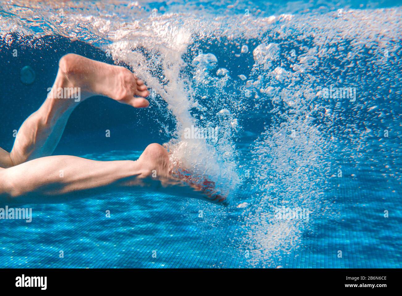 Men's legs swimming underwater in the swimming pool in summer Stock