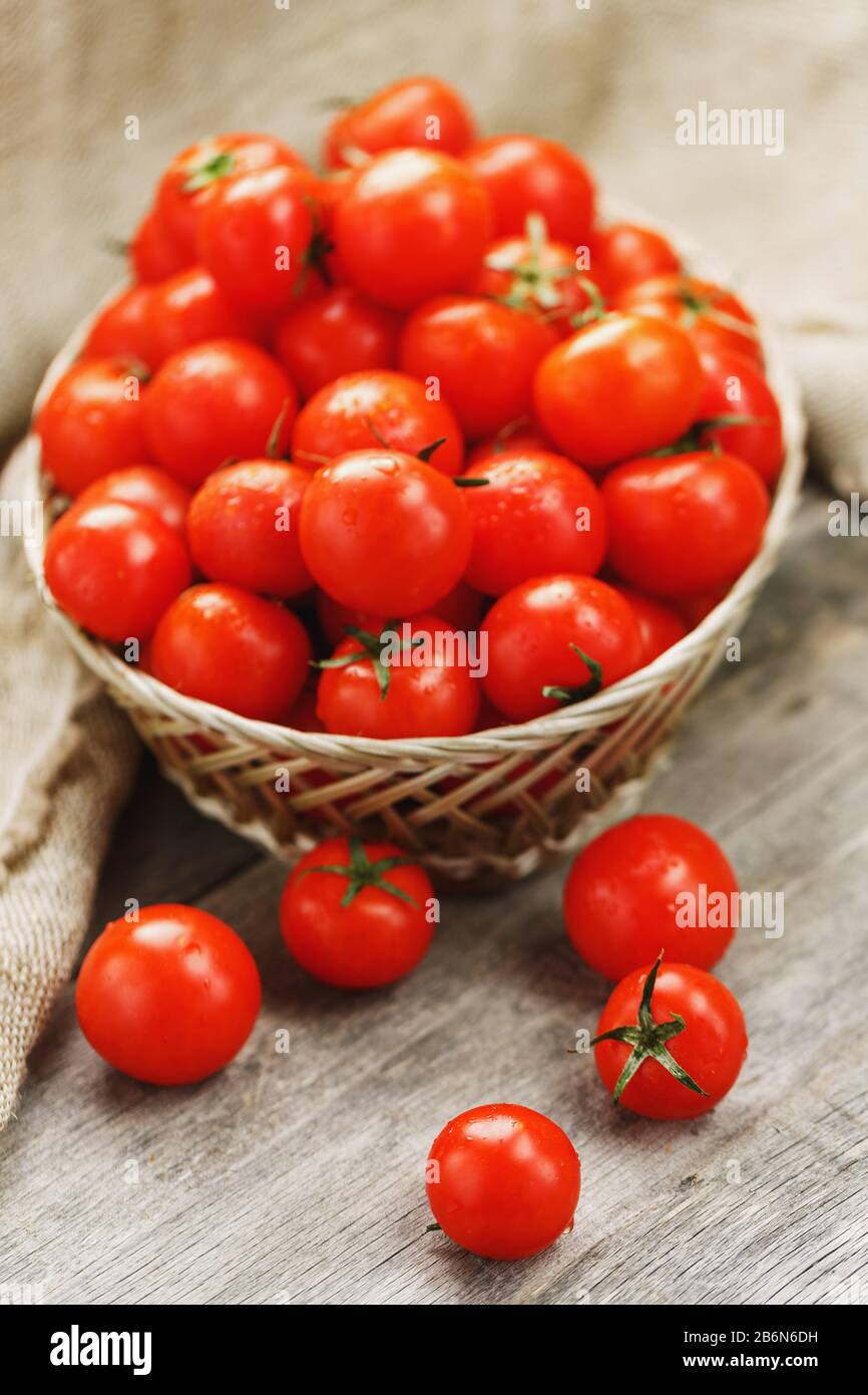 Small red tomatoes in a wicker basket on an old wooden table. Ripe and ...