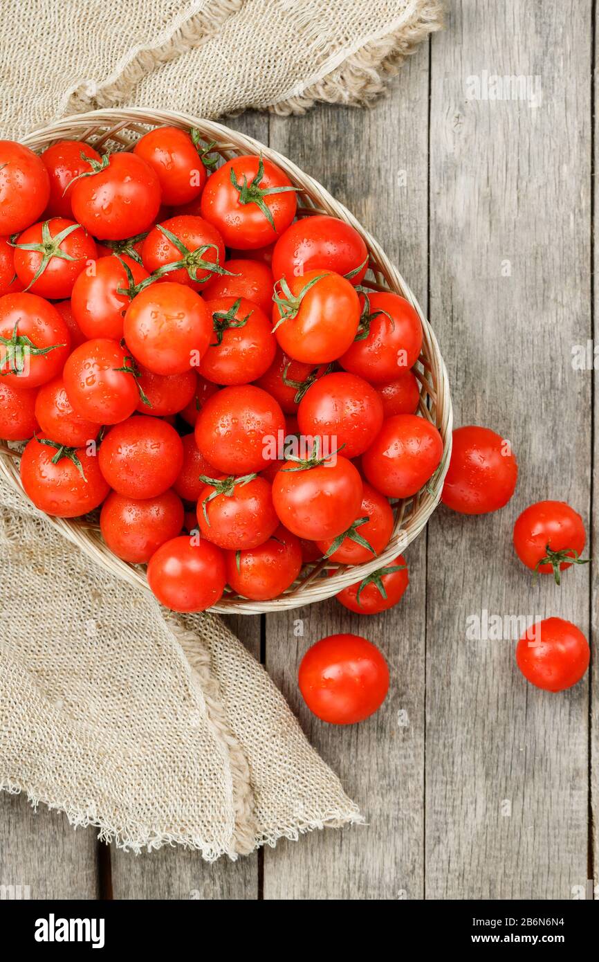 Small red tomatoes in a wicker basket on an old wooden table. Ripe and ...