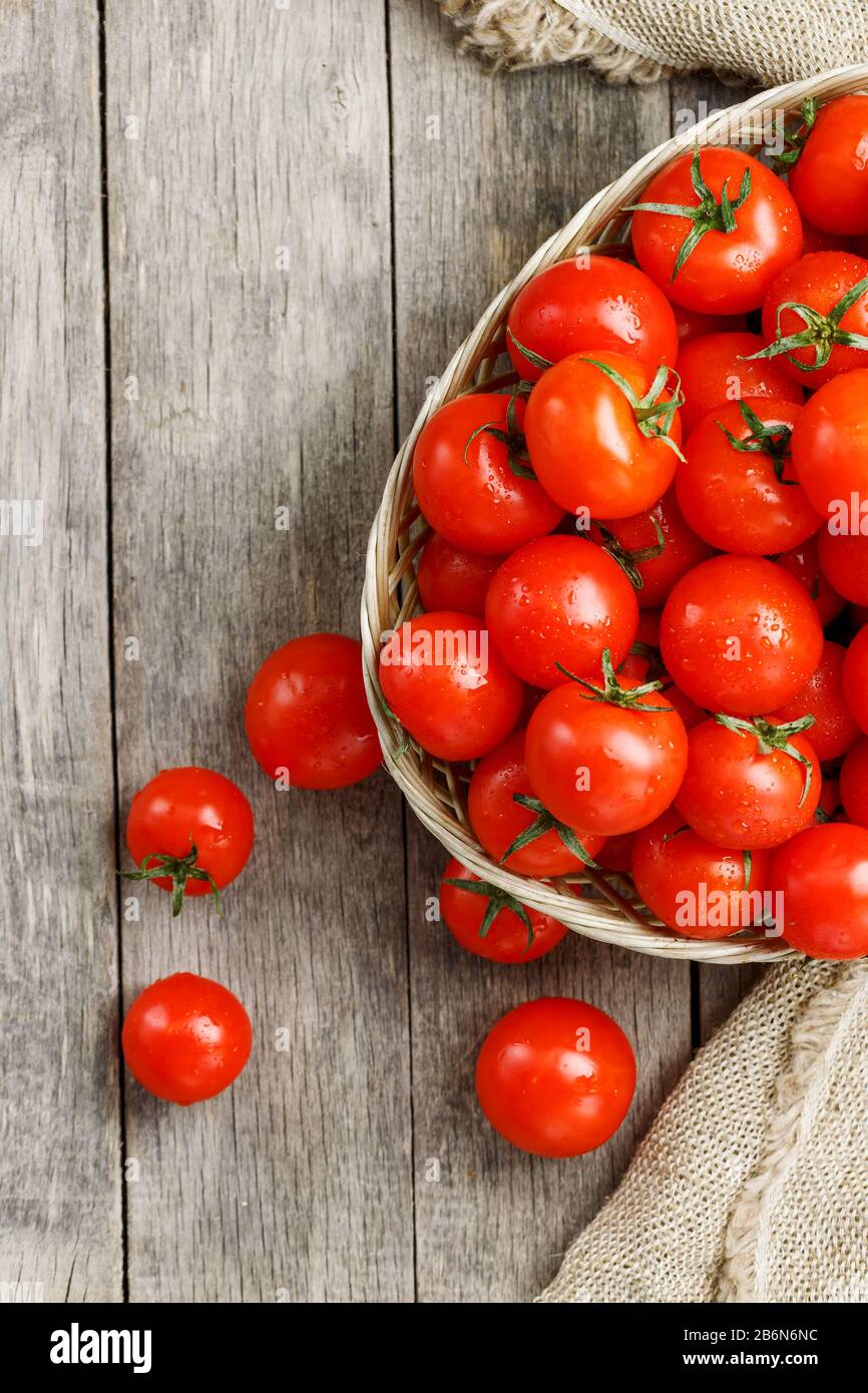 Small red tomatoes in a wicker basket on an old wooden table. Ripe and ...