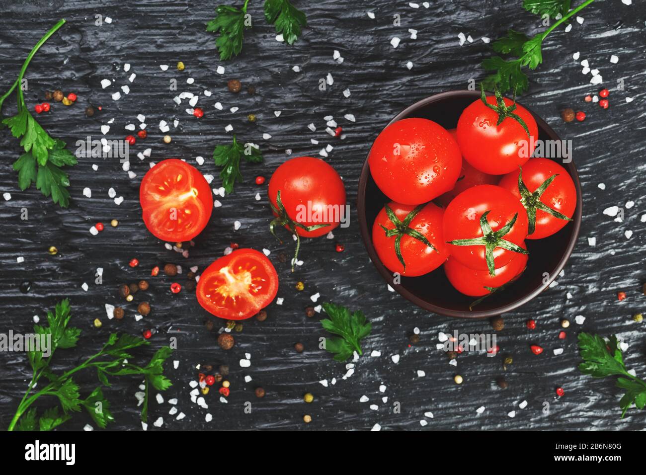 Fresh Sliced Cherry Tomatoes on a black background with spices coarse ...