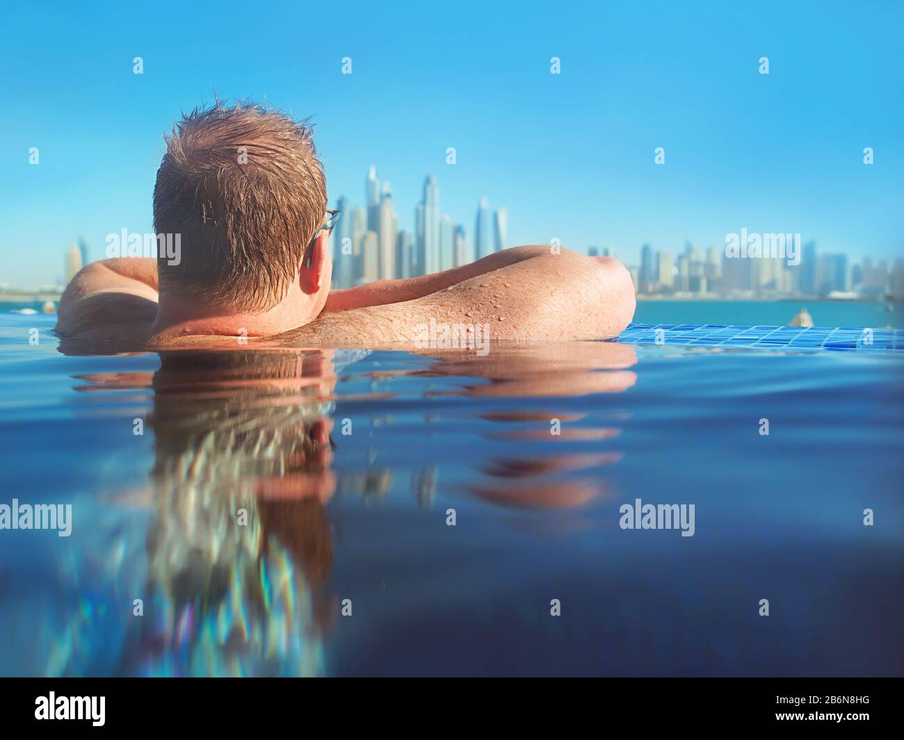 portrait of relaxed european caucasian redhead man with hair back in glasses in the swimming pool on modern Dubai (United Arabic Emirates) and sea bac Stock Photo