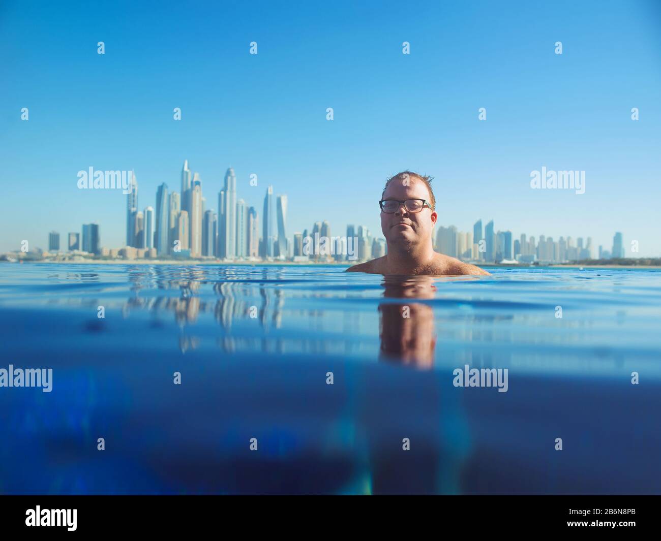 portrait of cheerful relaxed european caucasian redhead man in glasses in the swimming pool on modern Dubai (United Arabic Emirates)and sea background Stock Photo
