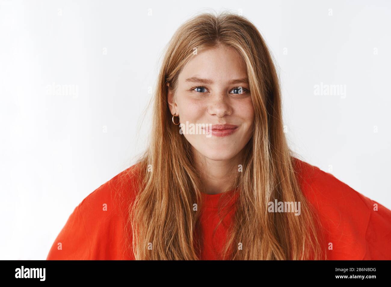 Portrait of friendly charismatic joyful female with long natural fair hair, freckles and cute chubby cheeks smiling happily posing against grey studio Stock Photo