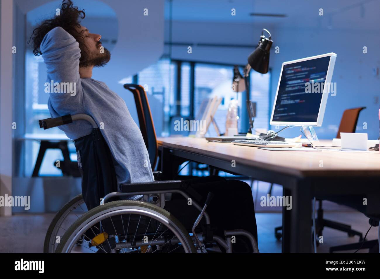 Disabled web developer in the wheelchair works in the office at the computer while performing in