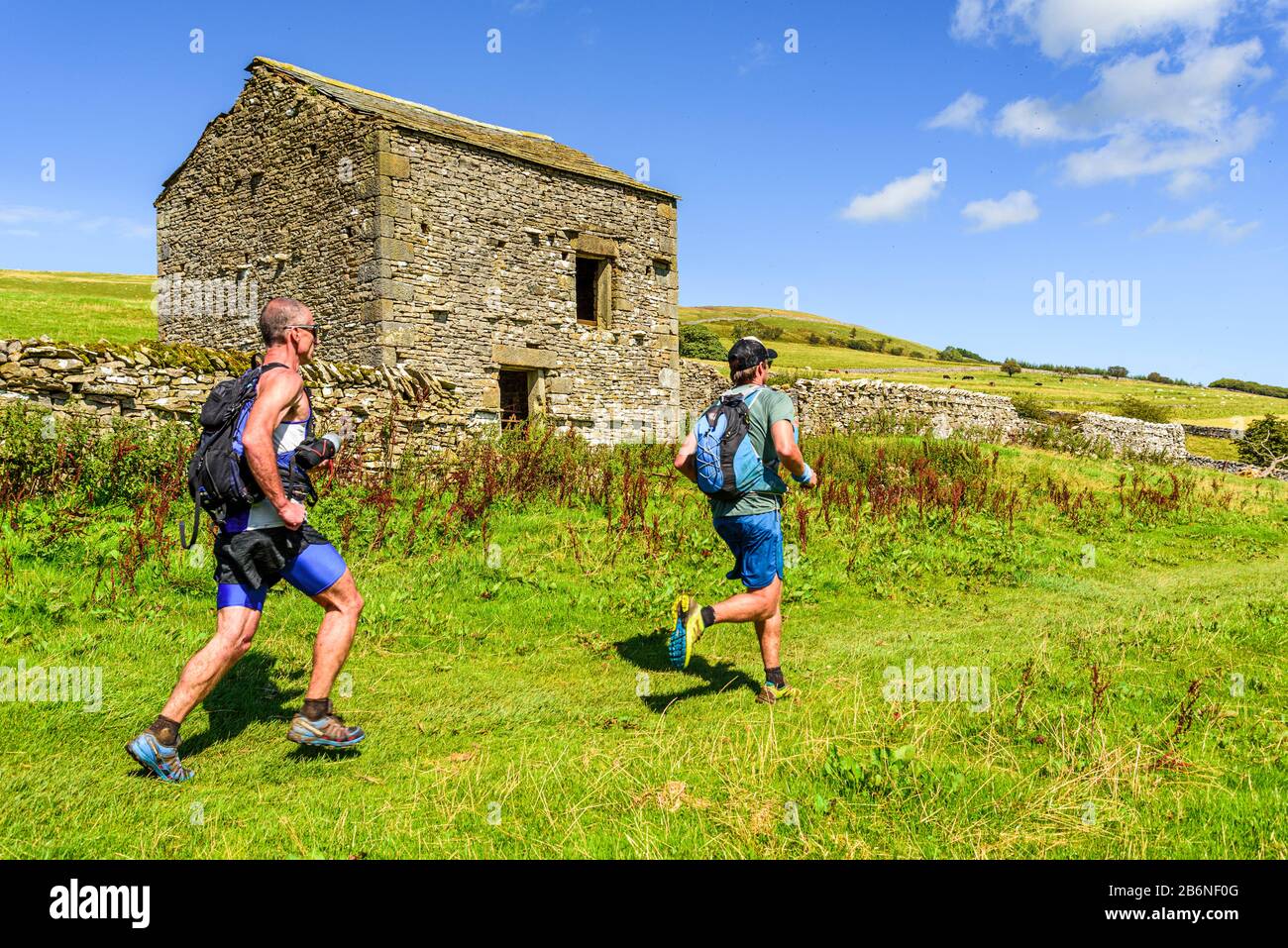 Fell runners pass an old barn near Orton in the Yorkshire Dales Stock Photo