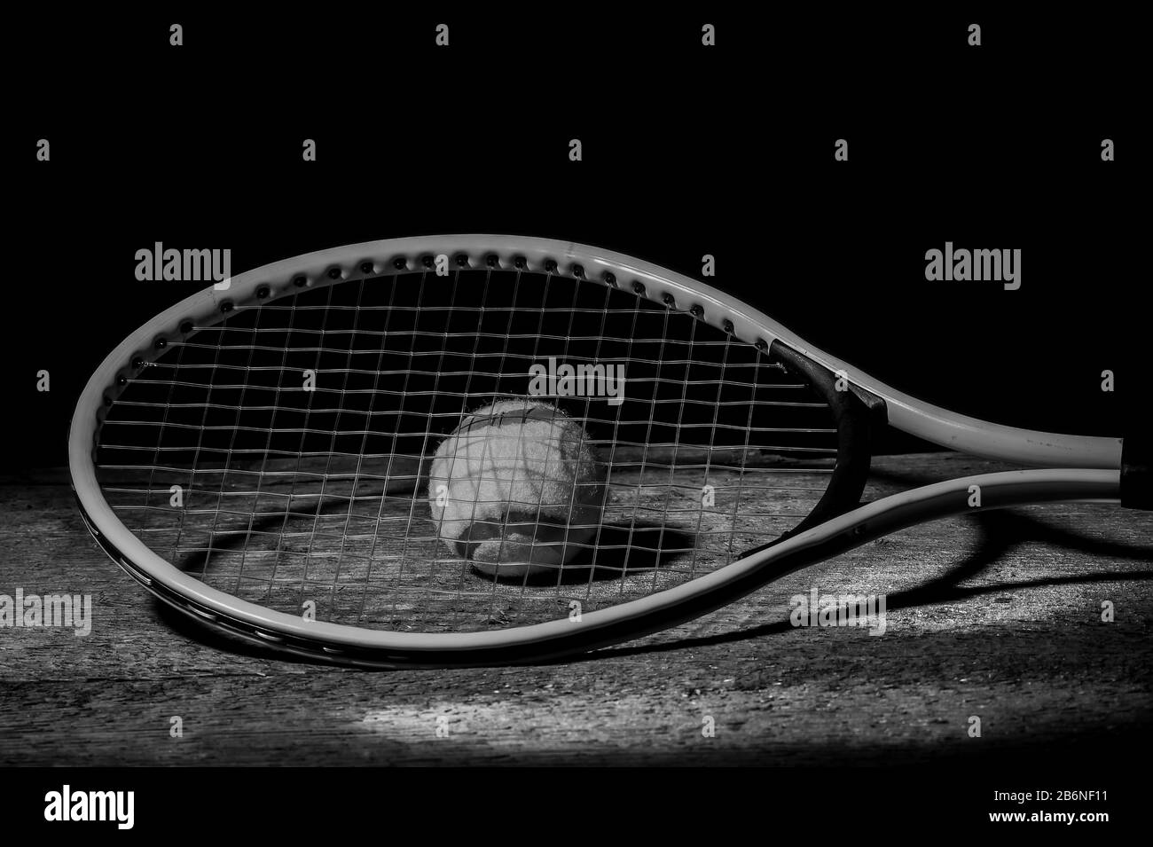 Tennis racket with tennis balls on wooden table with black background and copy space. Black and white Stock Photo