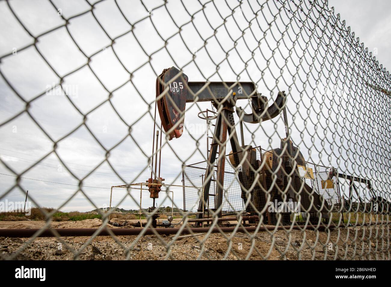 Oil Pump in Cloudy Rough Weather with Chain Link Fence Stock Photo