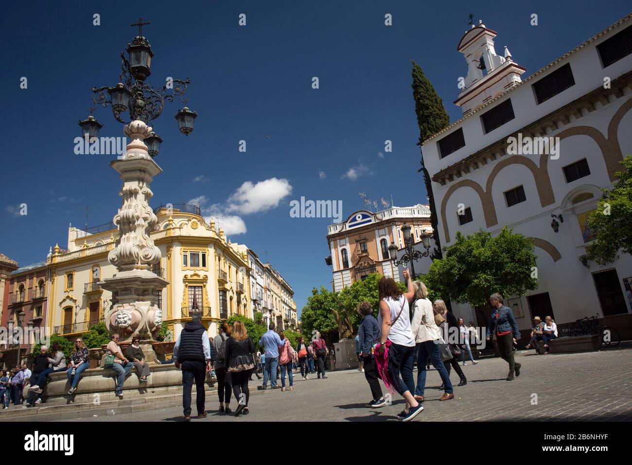 Passersby at Virgen de los Reyes Square with the fountain-lamppost and the Encarnación Convent as background, Seville, Spain Stock Photo