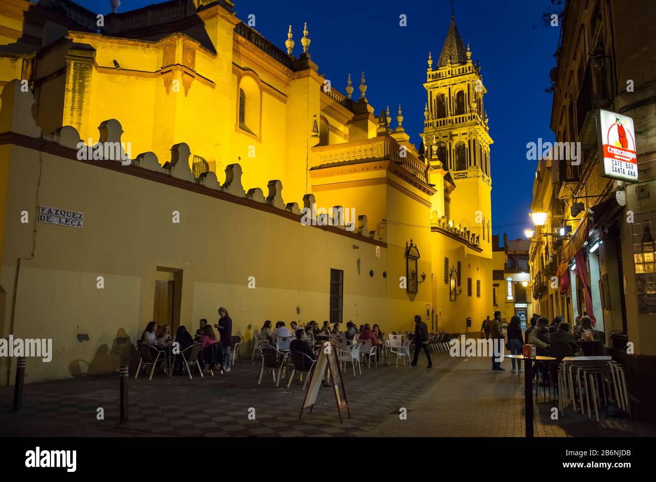 Night horizontal shot of Santa Ana church, surrounded by terraces of tapas' bars at Vazquez de Leca St in Triana district, Seville, Spain Stock Photo