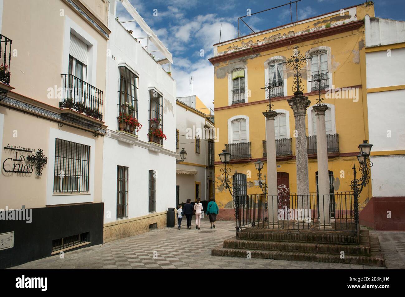 A family walking on Cruces Square in Santa Cruz district. There is a pedestal with three crosses in the middle of the square. Seville, Spain Stock Photo