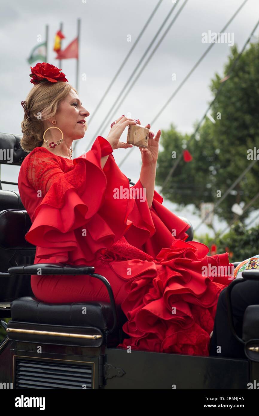 Lady wearing a Sevillian costume, sitting on a horse carriage and taking photos with her mobile phone in the Feria de Abril enclosure, Seville, Spain Stock Photo