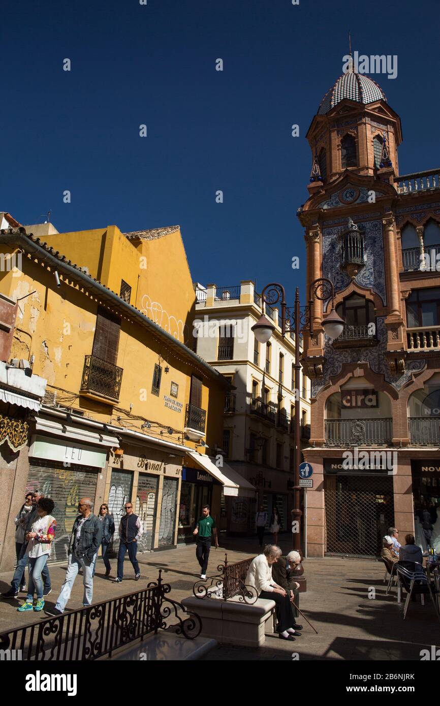 Colorful vertical shot of Jesus de la Pasion Square with passersby and an elderly couple sitting on a bench, Seville, Spain Stock Photo